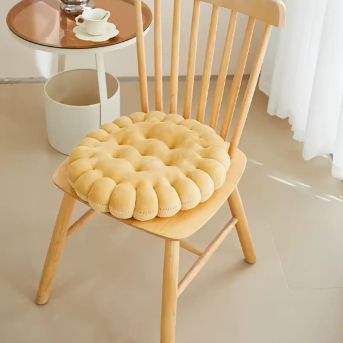 Coussin décoratif en forme de biscuit carré sur une chaise en bois à coté d'une petite table