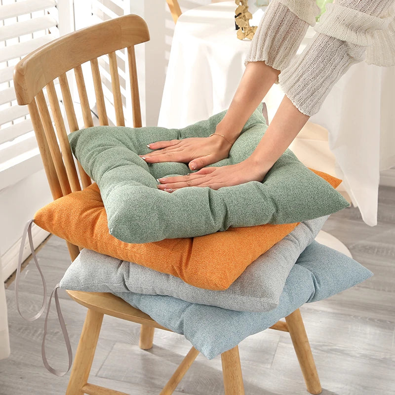Coussins carrés moelleux empilés sur une chaise en bois, mains appuyées pour montrer la souplesse de l’assise