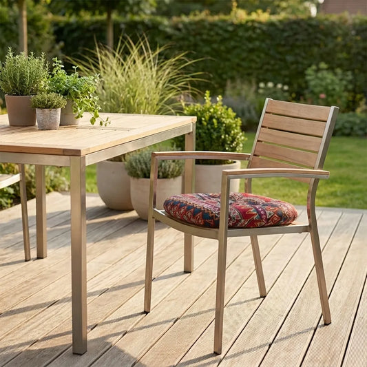Coussin de chaise rond à motif ethnique posé sur une chaise de jardin en métal et bois, installée sur une terrasse en bois clair avec une table assortie et des pots de plantes vertes en arrière-plan.
